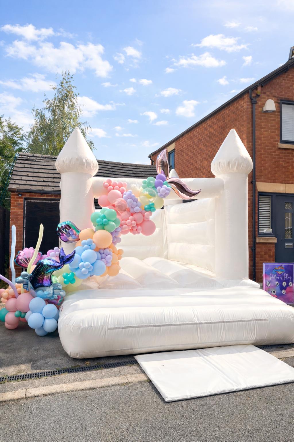 White luxury bouncy castle with unicorn rainbow balloon arch outdoors